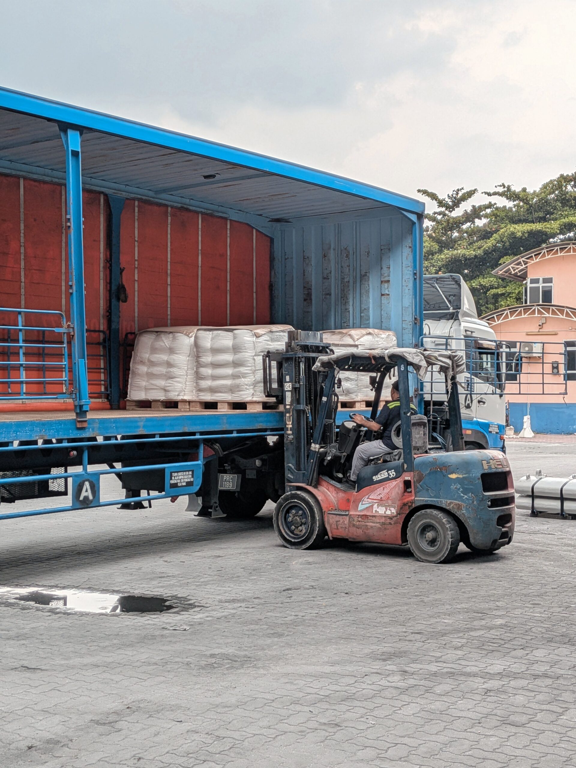 A forklift loading pallets into a truck outdoors in Ipoh, Malaysia. Industrial setting.